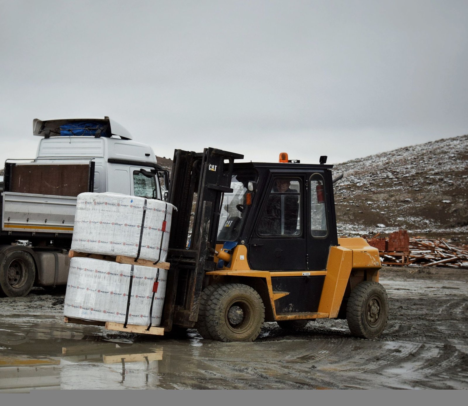 Forklift moving wrapped merchandise toward a freight truck at an industrial site